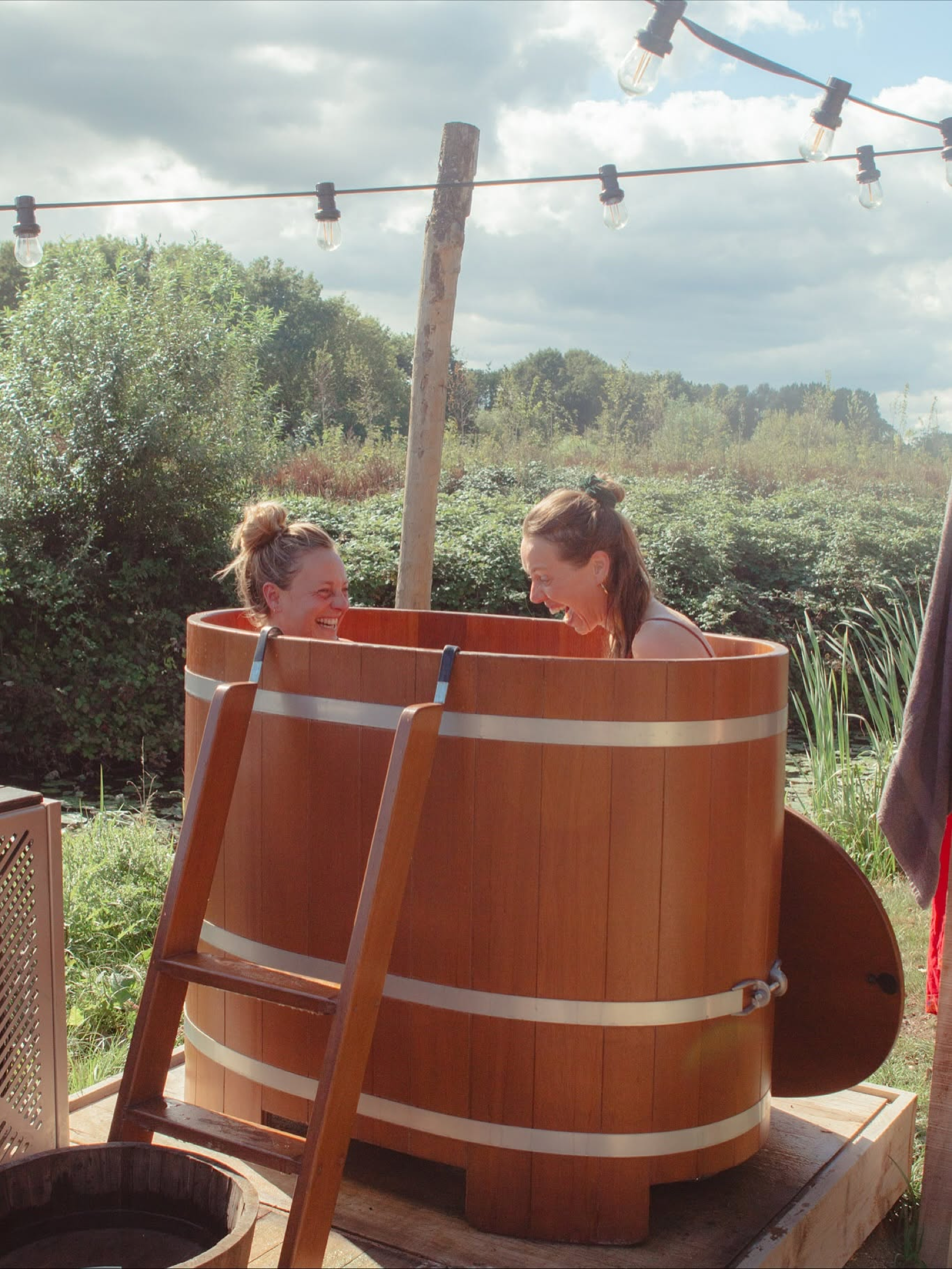 Twee deelnemers lachen samen in het dompelbad buiten bij Dankjewellness